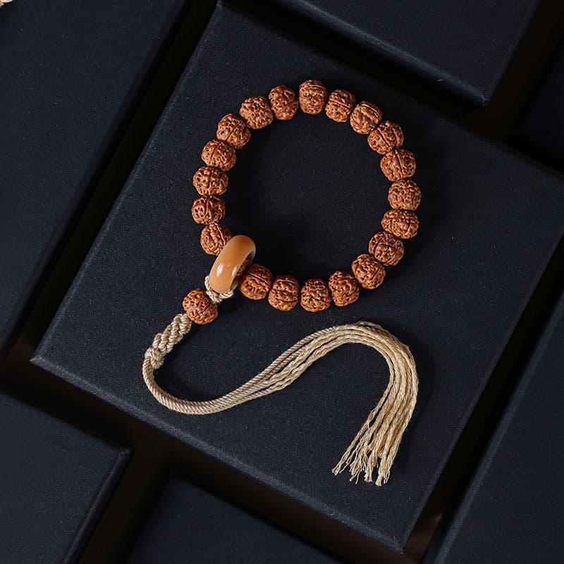 Rudraksha Bodhi bracelet with cylindrical accent bead and hemp tassel on dark surface