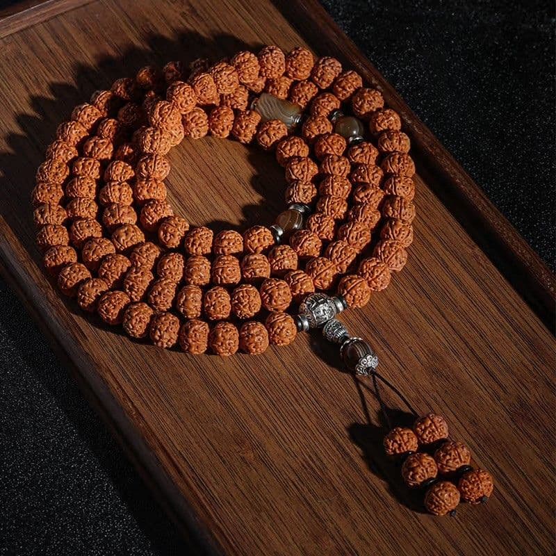 108-Bead Rudraksha Mala with a cream accent bead and small pendant on dark wood