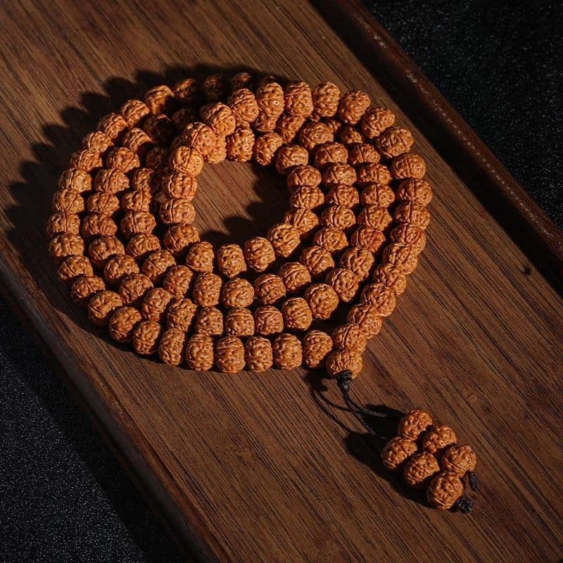108-Bead Rudraksha Mala with a small cream accent bead on dark wood