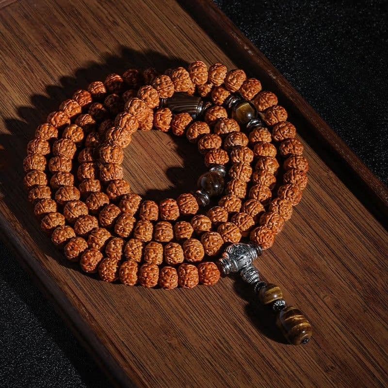 108-Bead Rudraksha Mala with an amber accent bead and small charm on dark wood